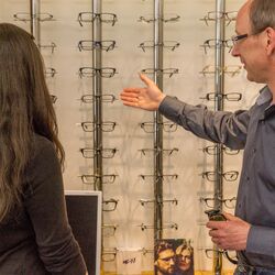 Beratungsgespräch: Der Optiker zeigt einer Kundin verschiedende Brillengestelle im Regal.